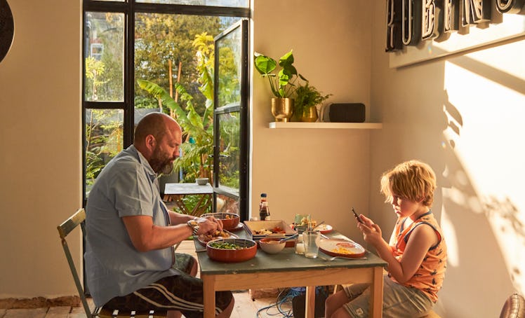 A mature father and young son are sitting at the dining table at home enjoying a meal together