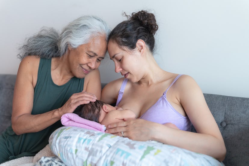 A happy young mom her infant daughter on a couch. Her mother is sitting next to her and she's workin...