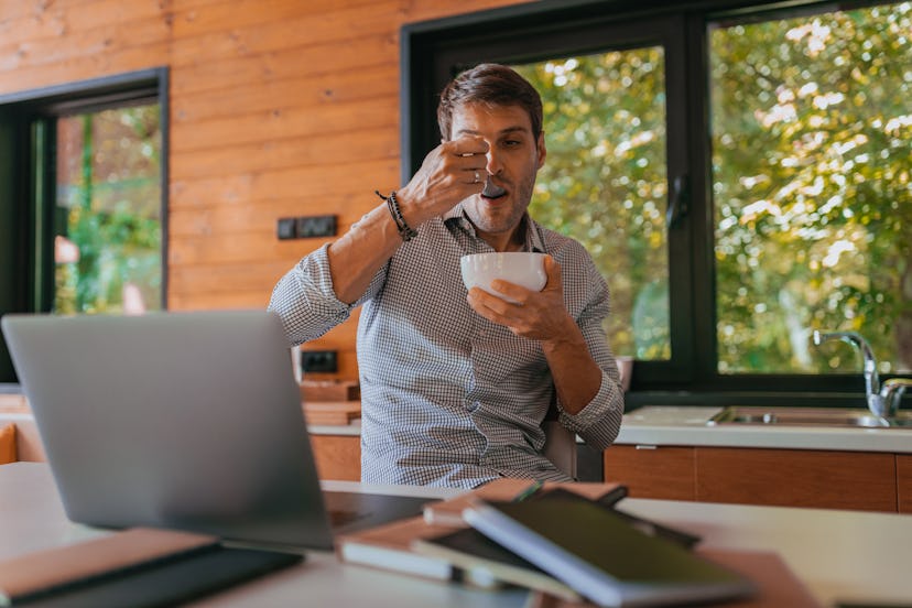 Portrait of young man enjoying eating while working at home.