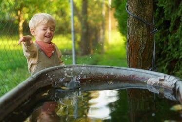 Happy little boy throwing rocks into the rainwater tank in the garden. Stone skipping game.