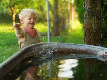 Happy little boy throwing rocks into the rainwater tank in the garden. Stone skipping game.