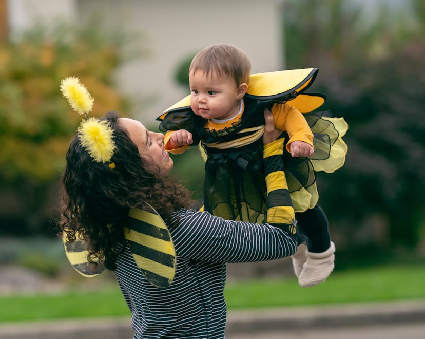 A beautiful mixed race mother in easy bumble bee costume holds her matching baby daughter up in the ...