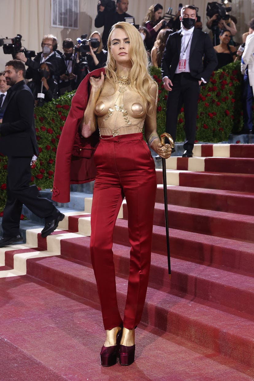 Cara Delevingne wears a red suit and gold pasties to attend "In America: An Anthology of Fashion," t...