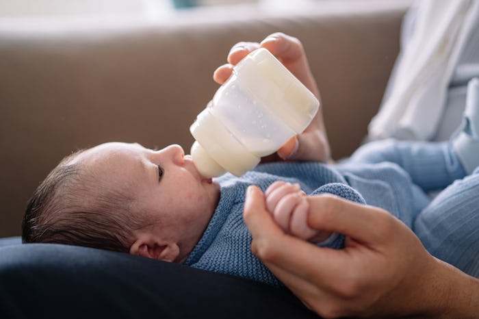 Horizontal cropped view of caucasian young father feeding maternal milk to baby boy at home. Family ...