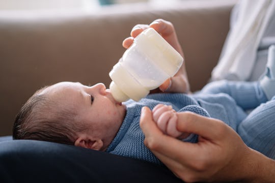 Horizontal cropped view of caucasian young father feeding maternal milk to baby boy at home. Family ...
