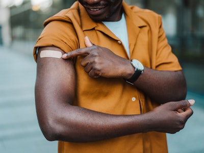 Cropped shot of man pointing at his arm with a bandage after receiving COVID-19 vaccine. Young man s...