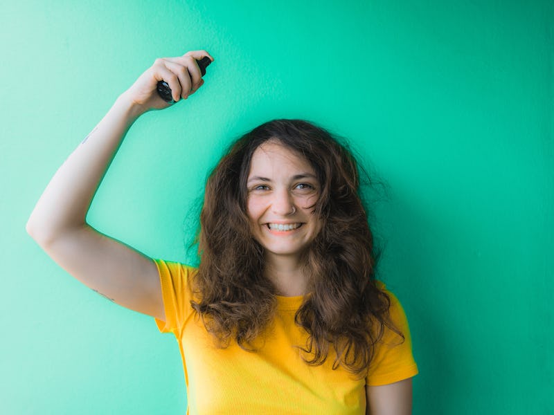 Young woman in yellow t-shirt trying to tame her frizzy curly hair and spraying hair care on it on ...