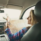 A mom in the shotgun seat of a car, looking at a map at tourist traps, as a dad drives.