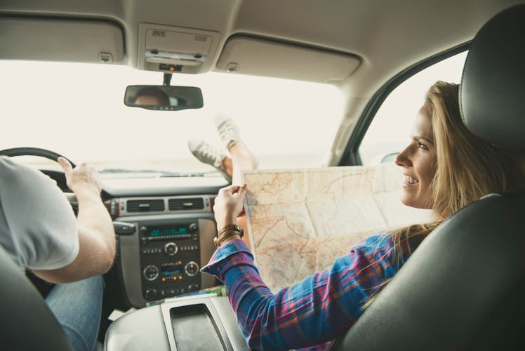 A mom in the shotgun seat of a car, looking at a map at tourist traps, as a dad drives.