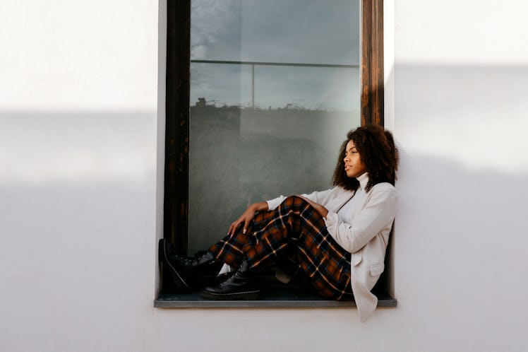 young woman sits in a window sill as she considers how jupiter retrograde 2023 will affect her zodia...