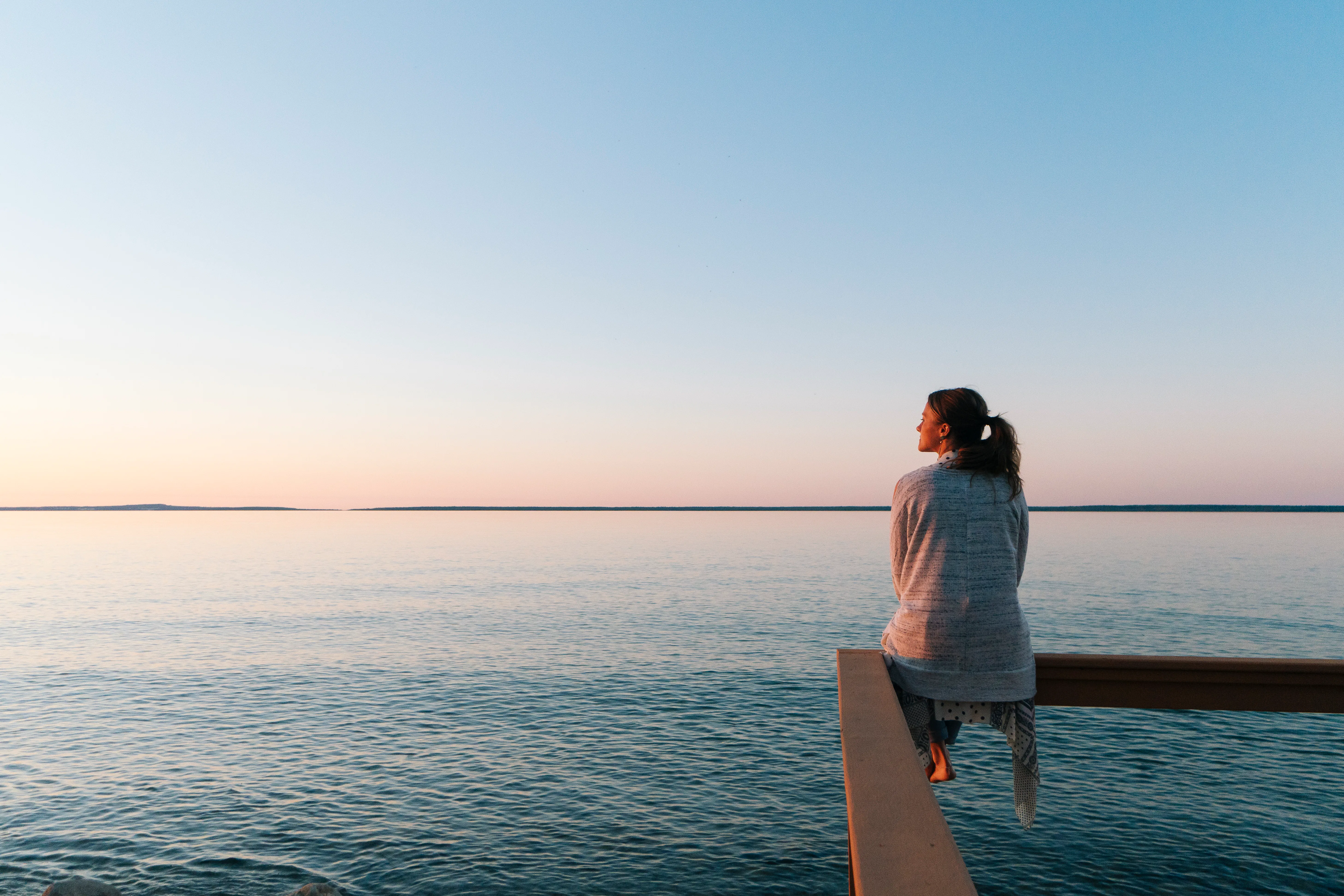 A woman wondering if she can manifest better mental health looks out at the water in meditation.