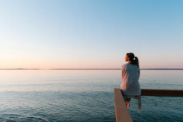 A woman wondering if she can manifest better mental health looks out at the water in meditation.