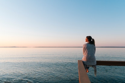 A woman wondering if she can manifest better mental health looks out at the water in meditation.