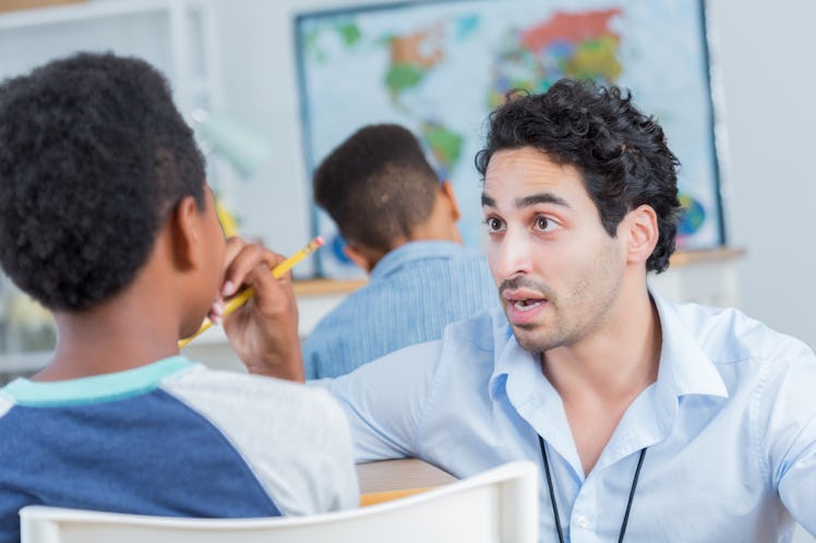 Serious male teacher helps or disciplines a male middle school student during class. The teacher has...