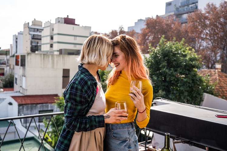 Lesbian couple relaxing and drinking wine on apartment's balcony