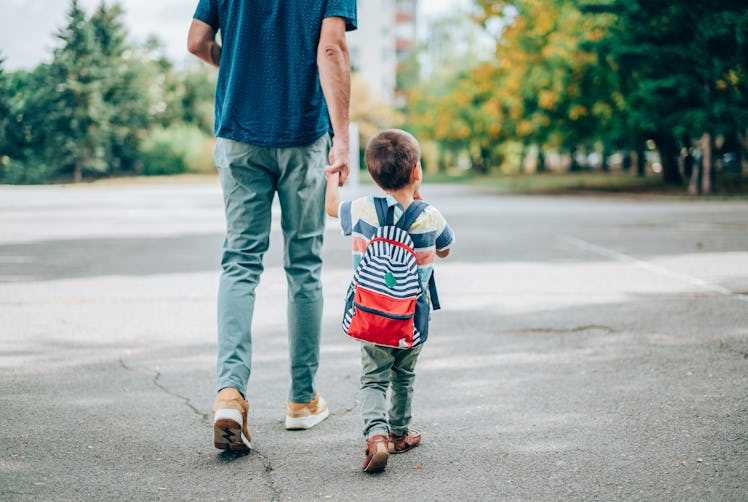 A dad walks his small child to school as they hold hands.