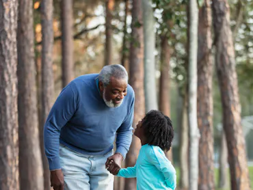 An African-American boy and his grandfather walking together in a park, holding hands, looking at ea...