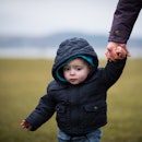 Image of a beautiful young boy being led by the hand in the park on a cold day by grandmother / adul...