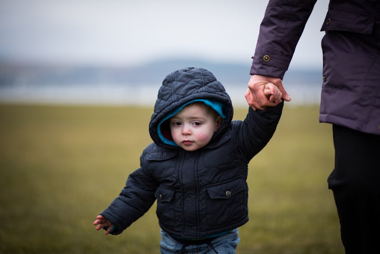 Image of a beautiful young boy being led by the hand in the park on a cold day by grandmother / adul...