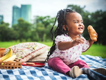 Little girl eating a croissant at a public park.
