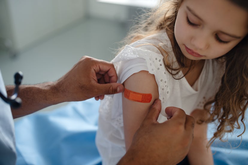 Doctor places bandage on girl's arm after administering a vaccine, in a story answering the question...