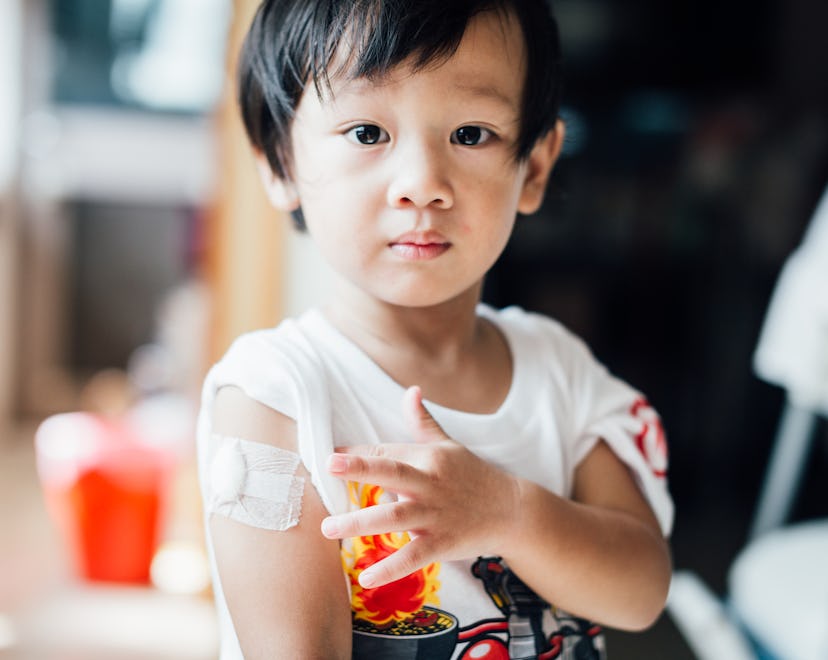 A toddler points to the bandage on his arm after a vaccine, in a story answering the question, is it...