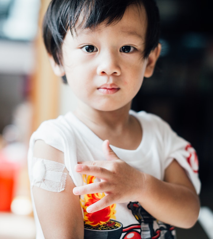A toddler points to the bandage on his arm after a vaccine, in a story answering the question, is it...