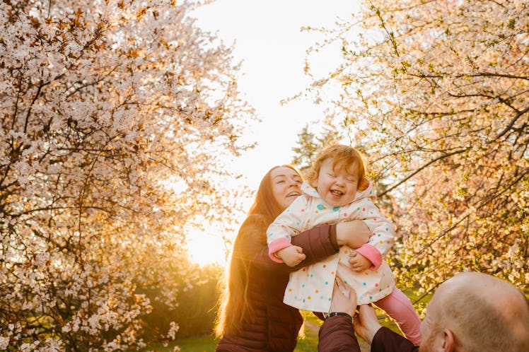 A parent holding their baby girl while surrounded by flowering trees.