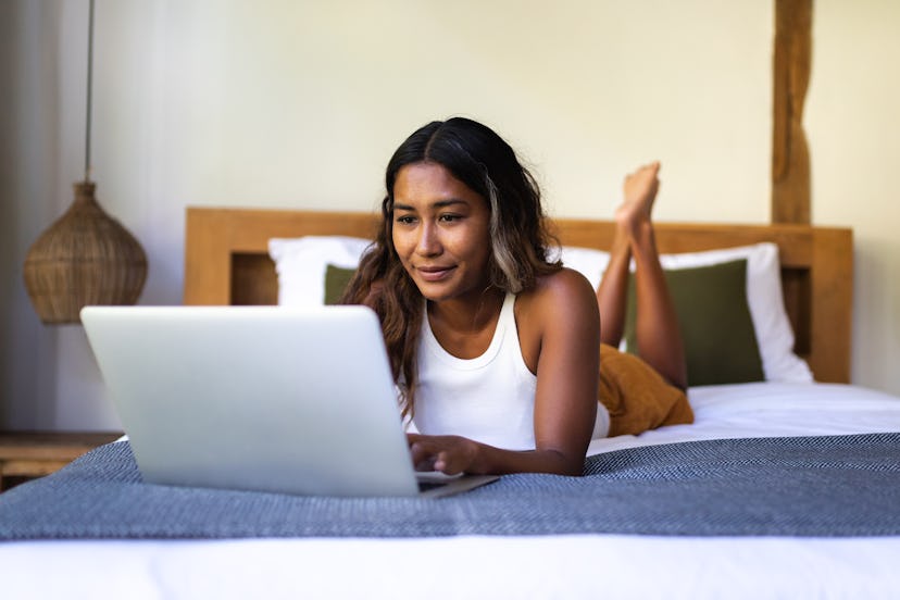 Asian Filipino woman using laptop lying on bed. Female relaxing at home. Technology and lifestyle co...