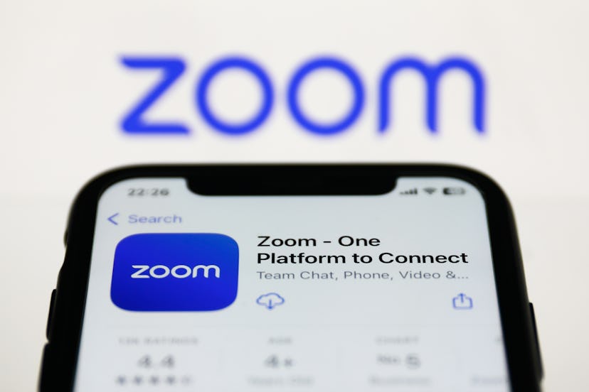 Zoom on App Store displayed on a phone screen and Zoom logo displayed on a screen in the background ...
