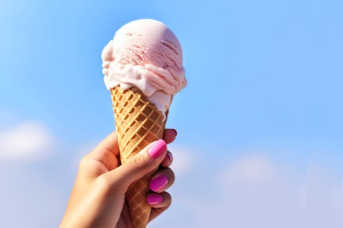 Female Hand holding of Juicy Ice Cream Cone in lavender pink color on blue sky background. Ice-cream...