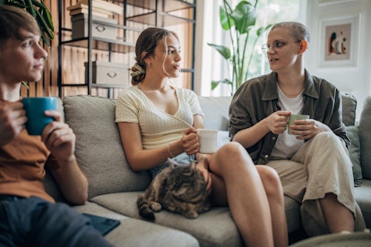 Three people, man and two women having coffee while sitting on sofa at home.