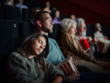 Young couple fell asleep during a boring movie in cinema. Focus is on woman.