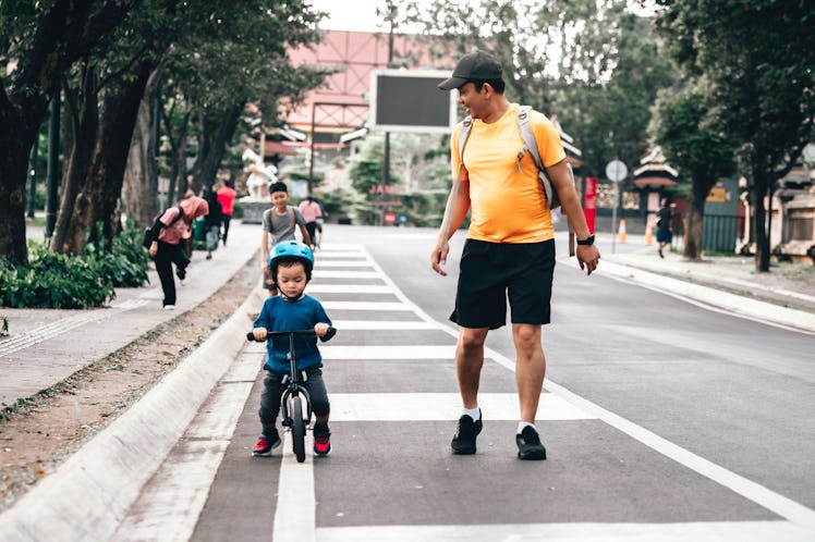 Father teaching son to ride a balanced bike walking down the street.