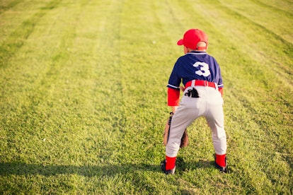 A young Little League baseball player wearing a baseball uniform is waiting for the next play to hap...