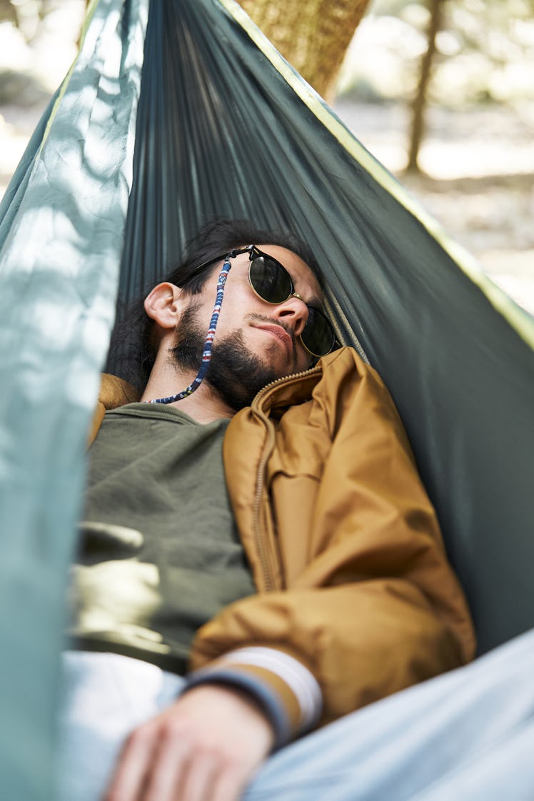 Vertical photo of a man sleeping on a hammock in a garden