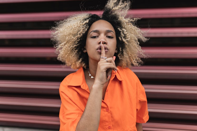 a young woman makes a "shh" gesture with her hand as she considers how Mercury retrograde 2023 will ...