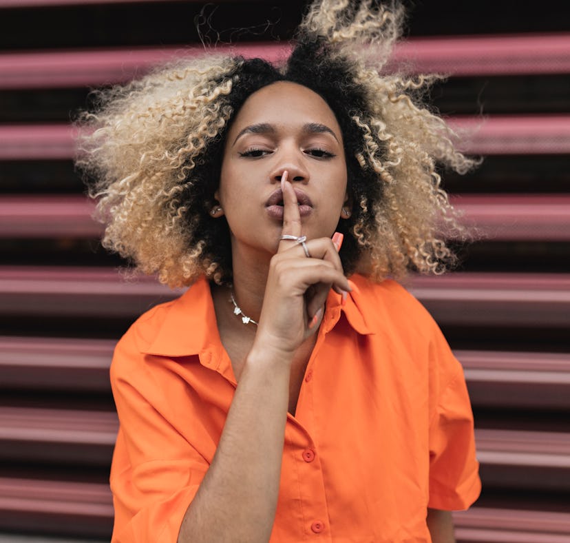 a young woman makes a "shh" gesture with her hand as she considers how Mercury retrograde 2023 will ...
