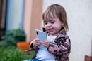 A cute baby girl with bangs is holding a massive smartphone in her hands and smiling