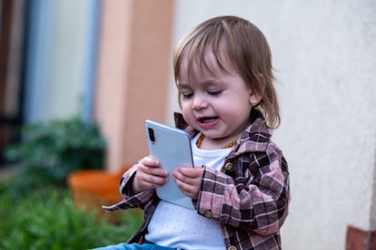A cute baby girl with bangs is holding a massive smartphone in her hands and smiling