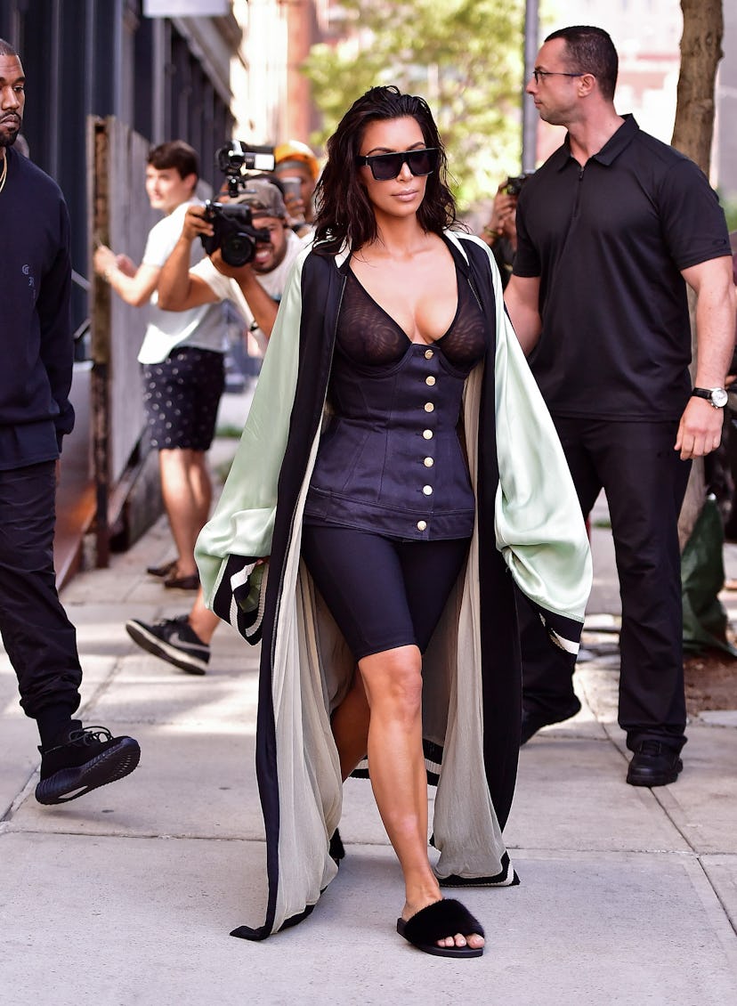 Kim Kardashian wears a sheer black corset over a bra, cycling shorts, fuzzy slides, and a kimono in …