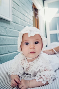Adorable and expressive baby girl with bonnet lying on her stomach, in article about girl names insp...