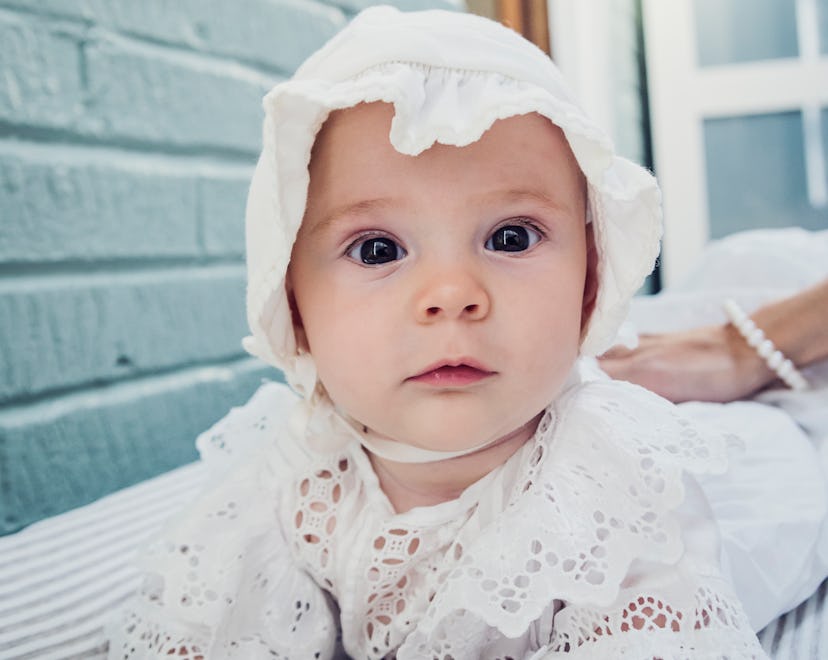 Adorable and expressive baby girl with bonnet lying on her stomach, in article about girl names insp...
