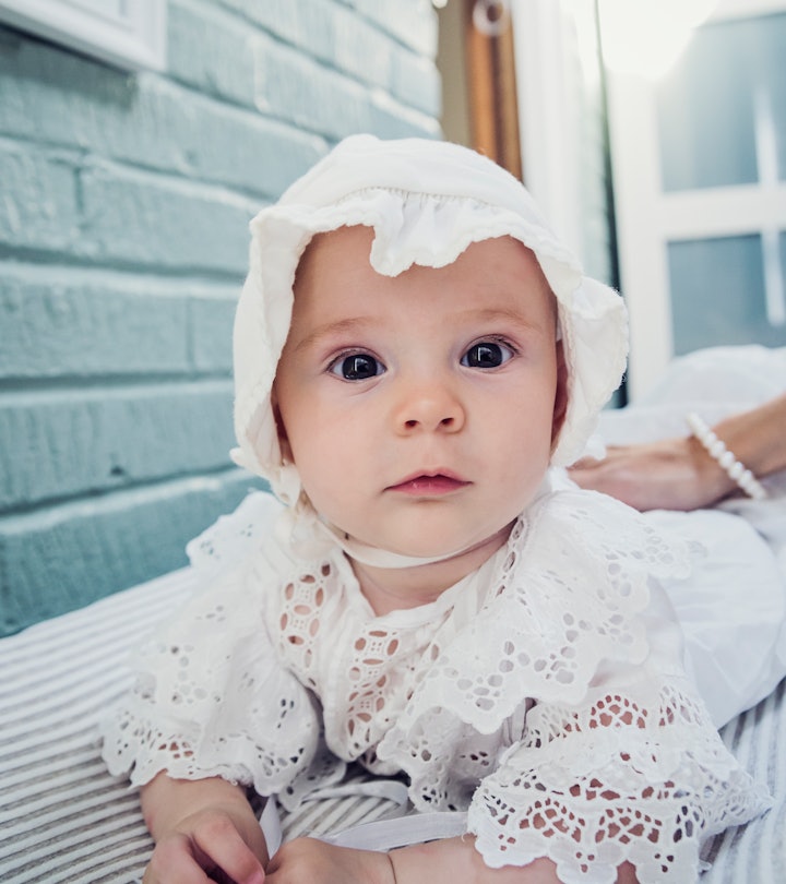 Adorable and expressive baby girl with bonnet lying on her stomach, in article about girl names insp...