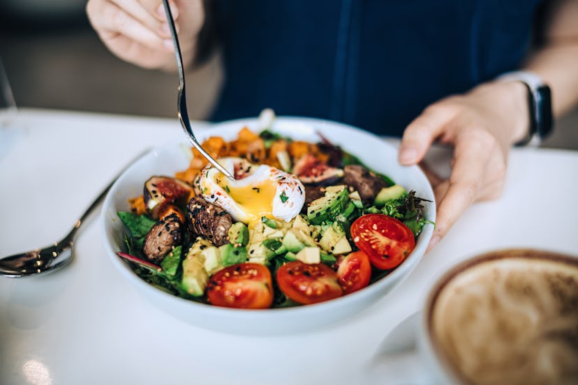 Close up shot of a woman eating a dish of fresh beef cobb salad with a soft boiled egg and coffee at...