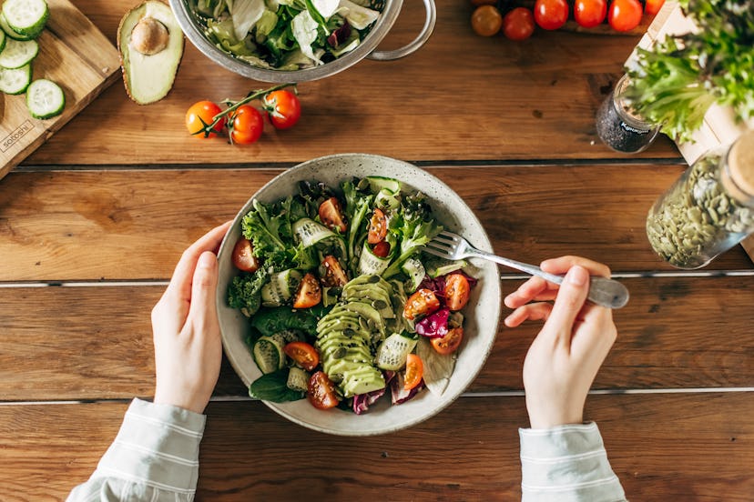 Woman hands holding fresh summer salad with raw vegetables cabbage, spinach, radish, parsley, greens...