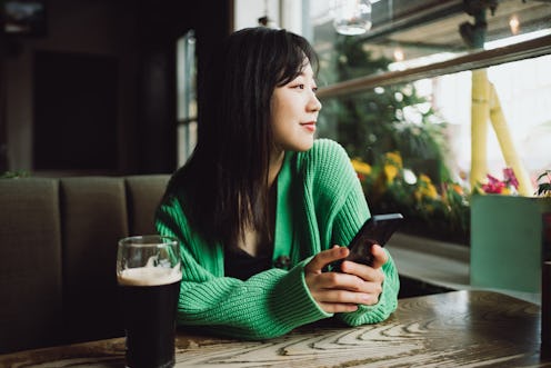 Asian beautiful woman holding her smartphone and looking outside in a restaurant.