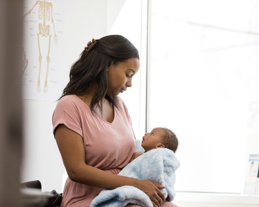 In the doctor's examination room, the depressed young adult mother looks down at her baby in her arm...