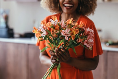 An unrecognizable black woman in an orange dress holding a bouquet of pink and orange flowers.