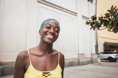 Portrait of a beautiful young African woman in a city looking at the camera. She is positive, toothy...